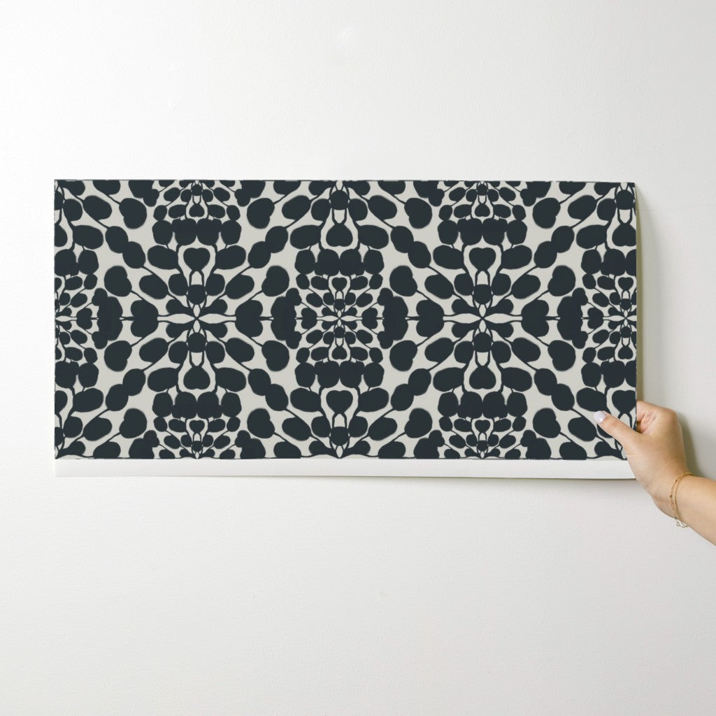 Hand holding a wallpaper swatch with a black floral pattern on a white background. Designed by artist Leila Simon Hayes.