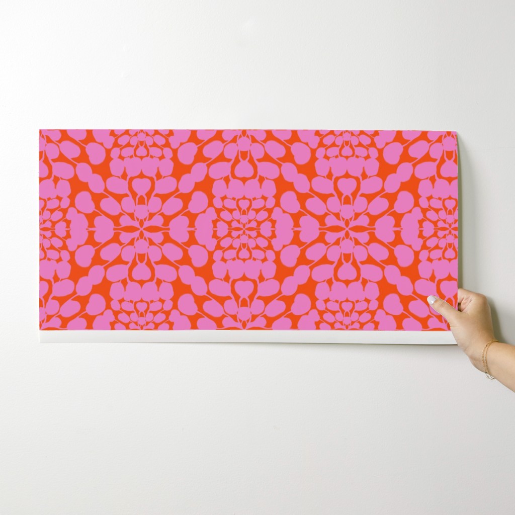 Hand holding a wallpaper swatch with a pink and orange pattern against a white background. Designed by artist Leila Simon Hayes. 