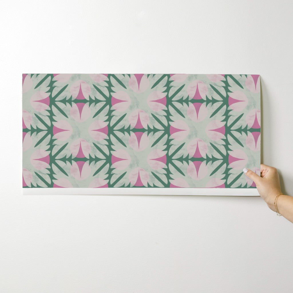 Hand holding a wallpaper swatch with a pink and green geometric pattern on a white background. Designed by artist Leila Simon Hayes. 