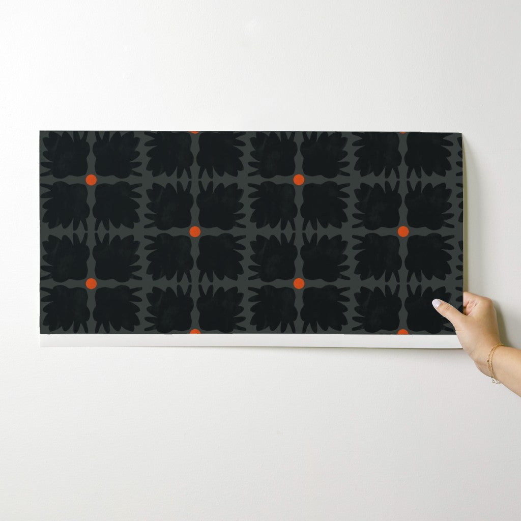 Hand holding a black and orange patterned wallpaper swatch against a white background. Designed by artist Leila Simon Hayes.