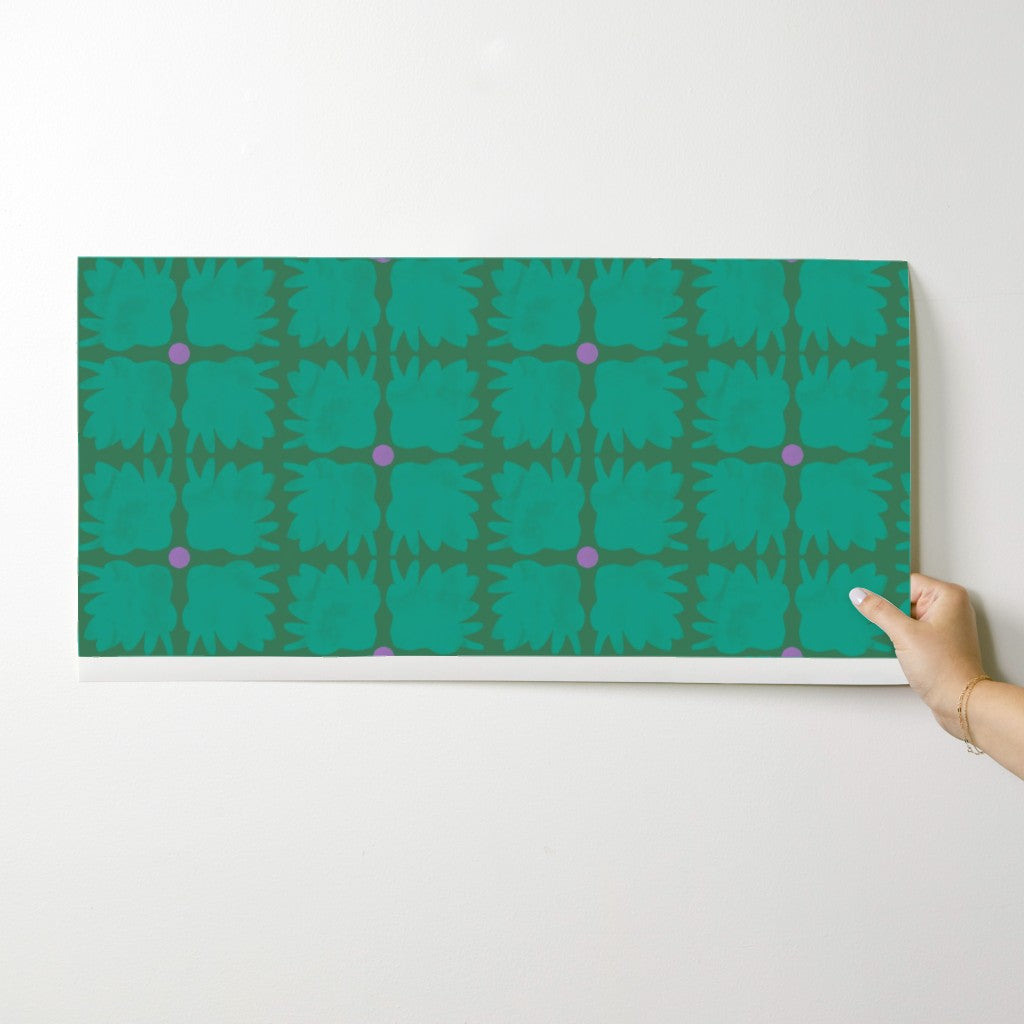 Hand holding a green patterned wallpaper swatch against a white background. Designed by artist Leila Simon Hayes.