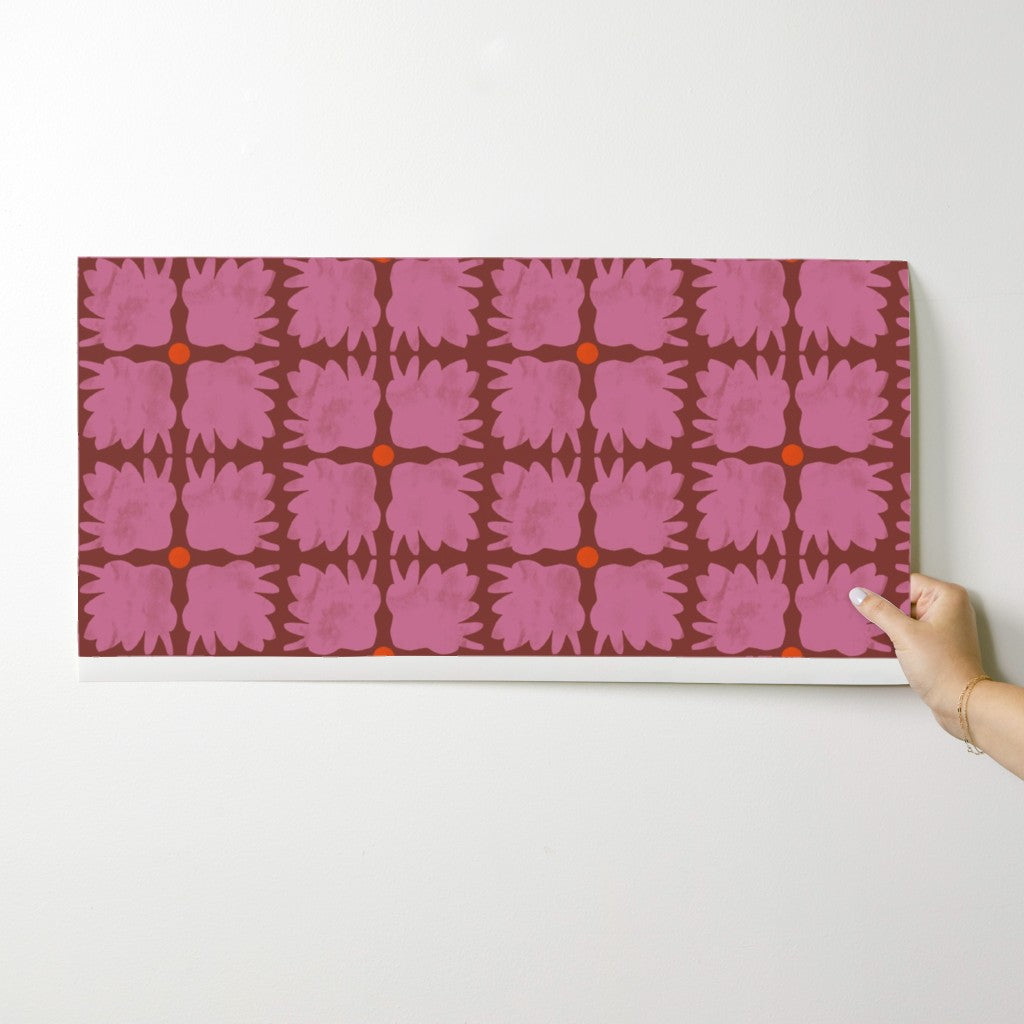 Hand holding a wallpaper swatch with pink floral pattern on a white background. Designed by artist Leila Simon Hayes.