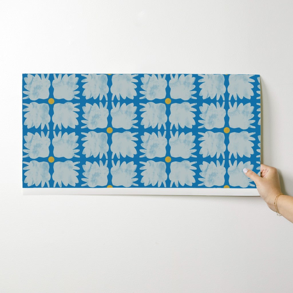 Hand holding a blue and white patterned wallpaper swatch on a white surface. Designed by artist Leila Simon Hayes.