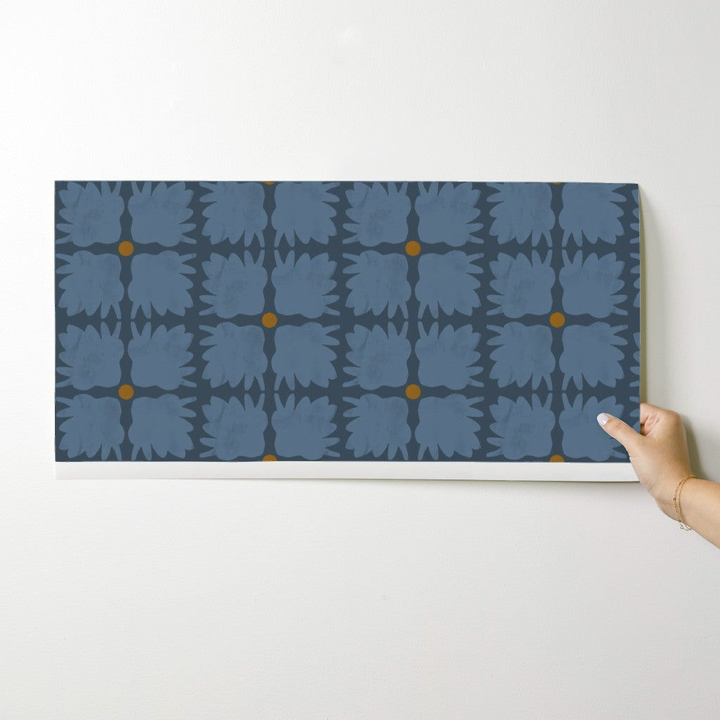 Hand holding a wallpaper swatch with blue floral pattern on a white background. Designed by artist Leila Simon Hayes.