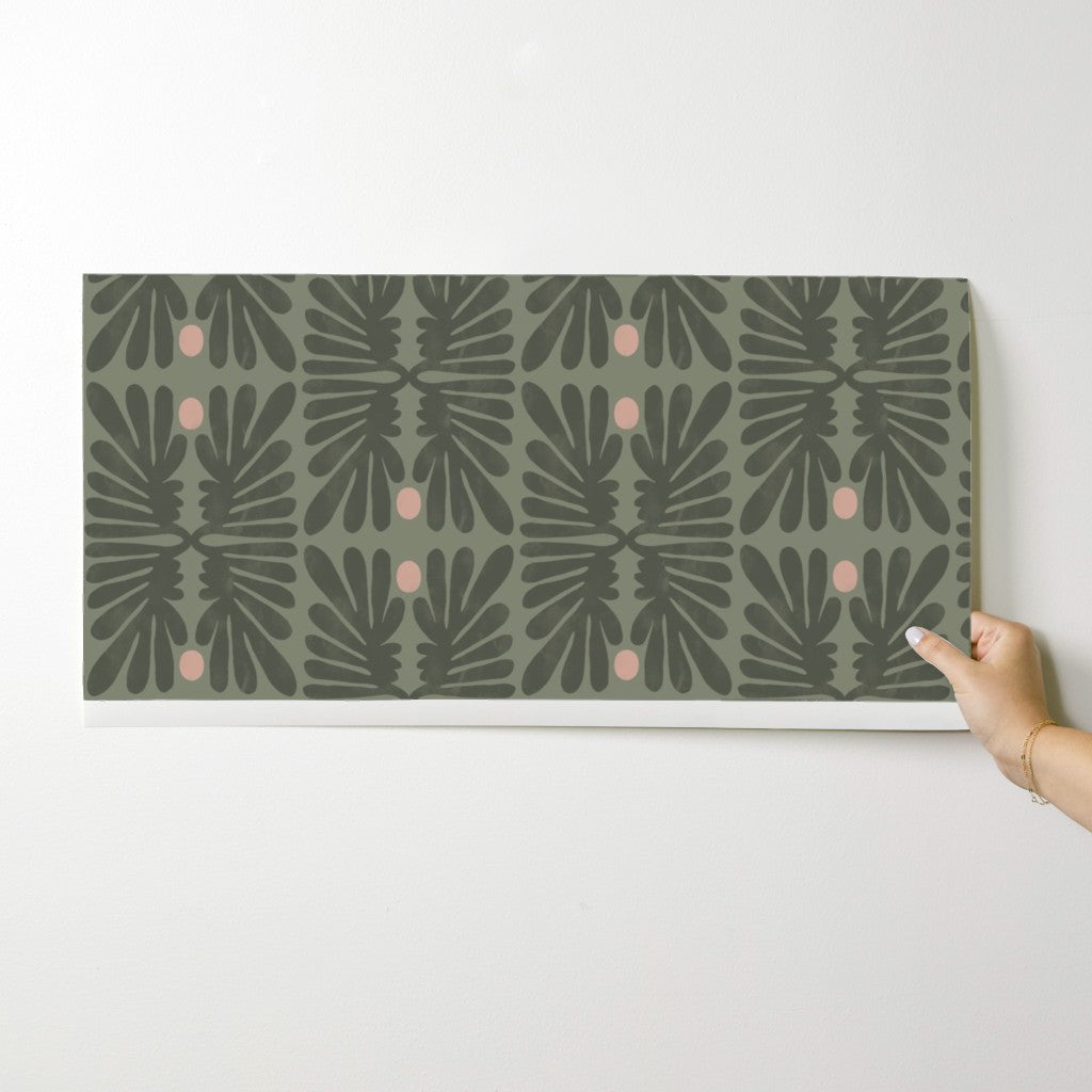 Hand holding a wallpaper swatch with a geometric pattern on a white background. Designed by artist Leila Simon Hayes. 