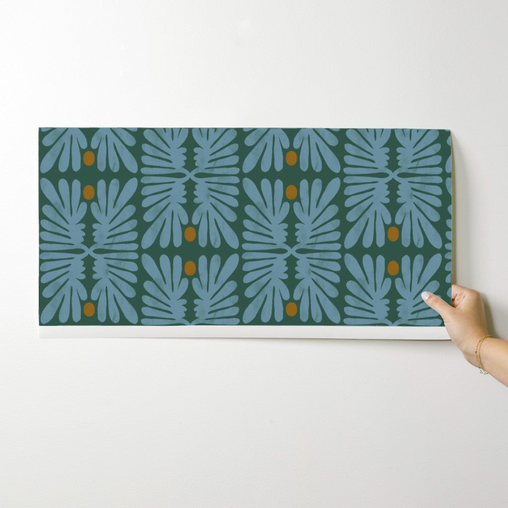 Hand holding a wallpaper swatch with a blue leaf pattern against a white background. Designed by artist Leila Simon Hayes. 