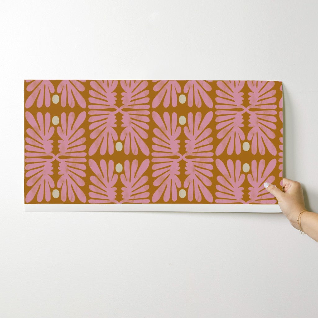 Hand holding a wallpaper swatch with pink leaf pattern on a white background. Designed by artist Leila Simon Hayes. 