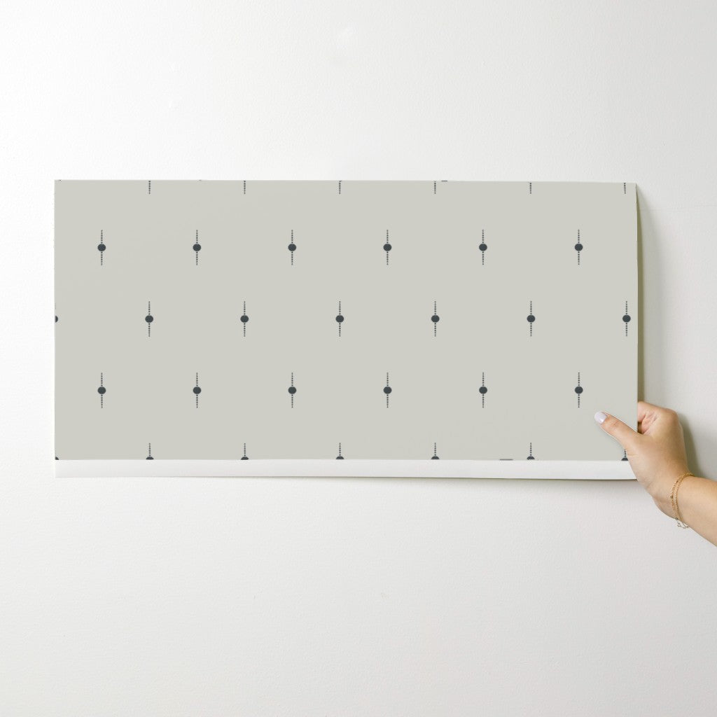 Person holding a sheet of white wallpaper with black geometric star patterns against a white background. Designed by artist Leila Simon Hayes. 
