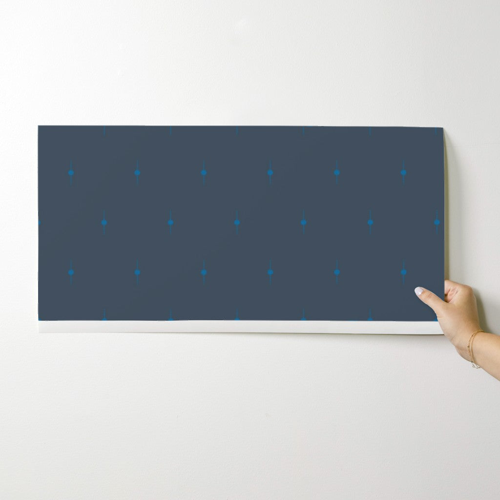 Hand holding a dark blue wallpaper swatch with small white dots on a light gray background. Designed by artist Leila Simon Hayes. 