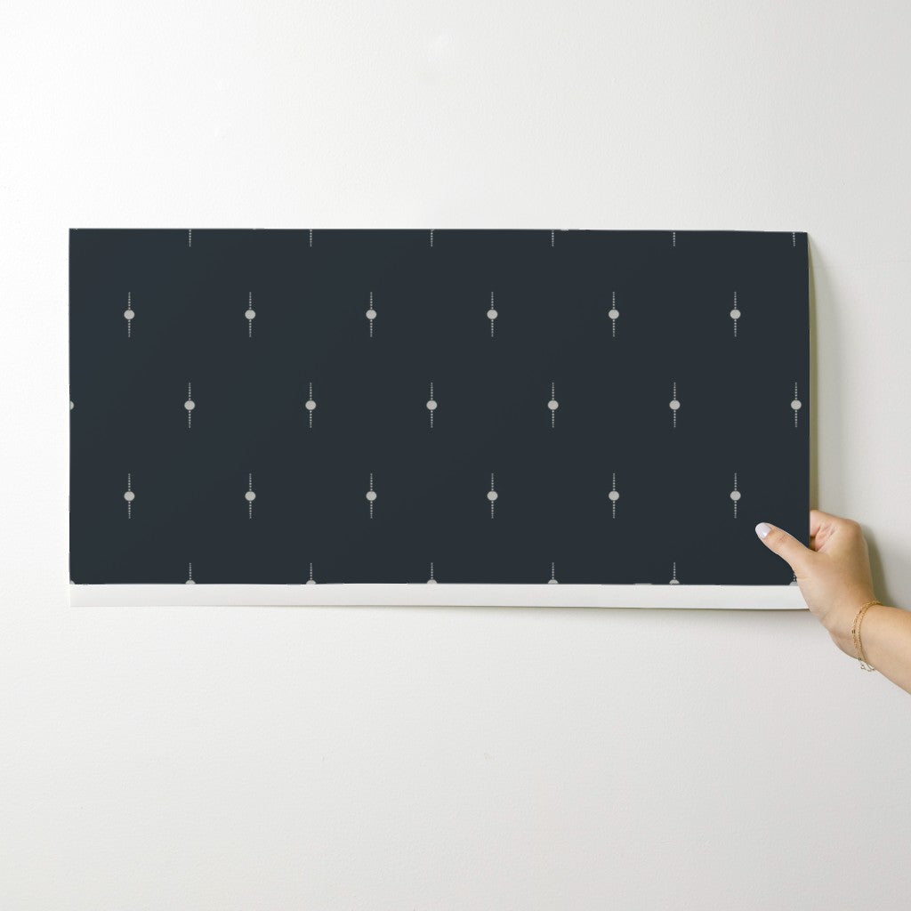 Black wallpaper swatch with white geometric pattern held by a hand on a light gray background. Designed by artist Leila Simon Hayes. 