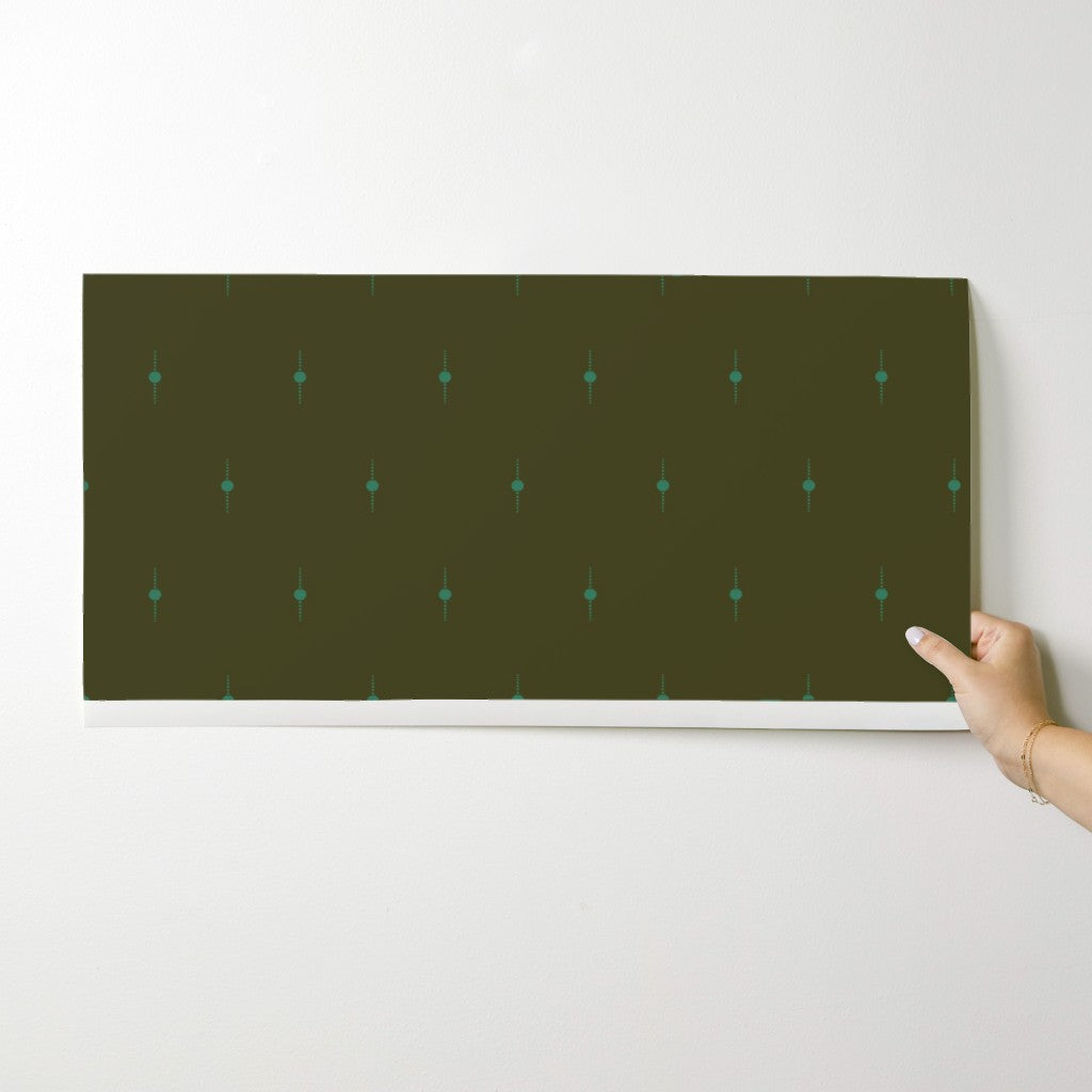 Hand holding a dark wallpaper swatch with a subtle geometric star pattern on a light gray background. Designed by artist Leila Simon Hayes. 