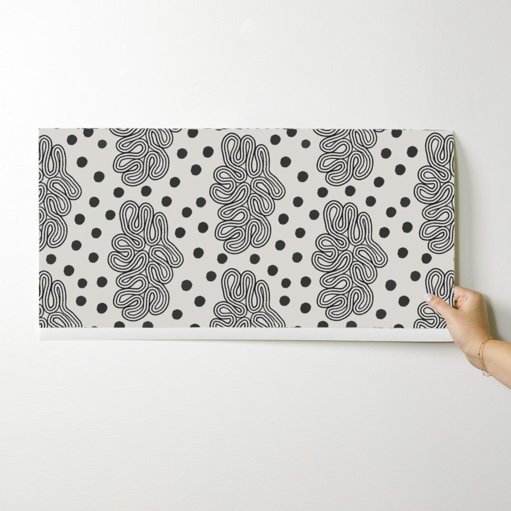 Person holding a wallpaper swatch with black and white abstract pattern on a white background. Designed by artist Leila Simon Hayes. 