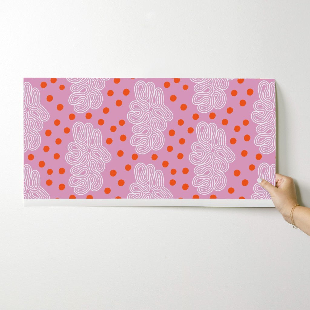Hand holding a pink patterned paper with white and red designs on a white background. Designed by artist Leila Simon Hayes. 