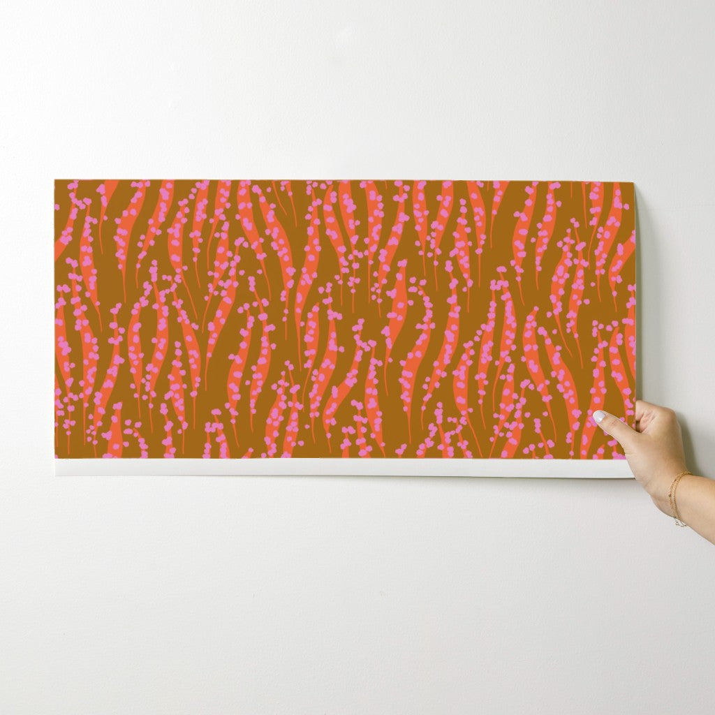 Hand holding a wallpaper swatch with a pink and orange abstract pattern on a white background. Designed by artist Leila Simon Hayes. 