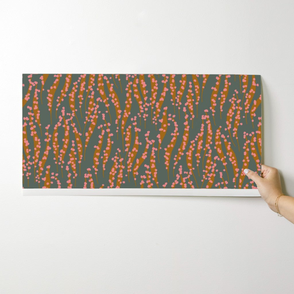 Hand holding a wallpaper swatch with a pattern of wavy lines in pink and orange on a gray background. Designed by artist Leila Simon Hayes. 