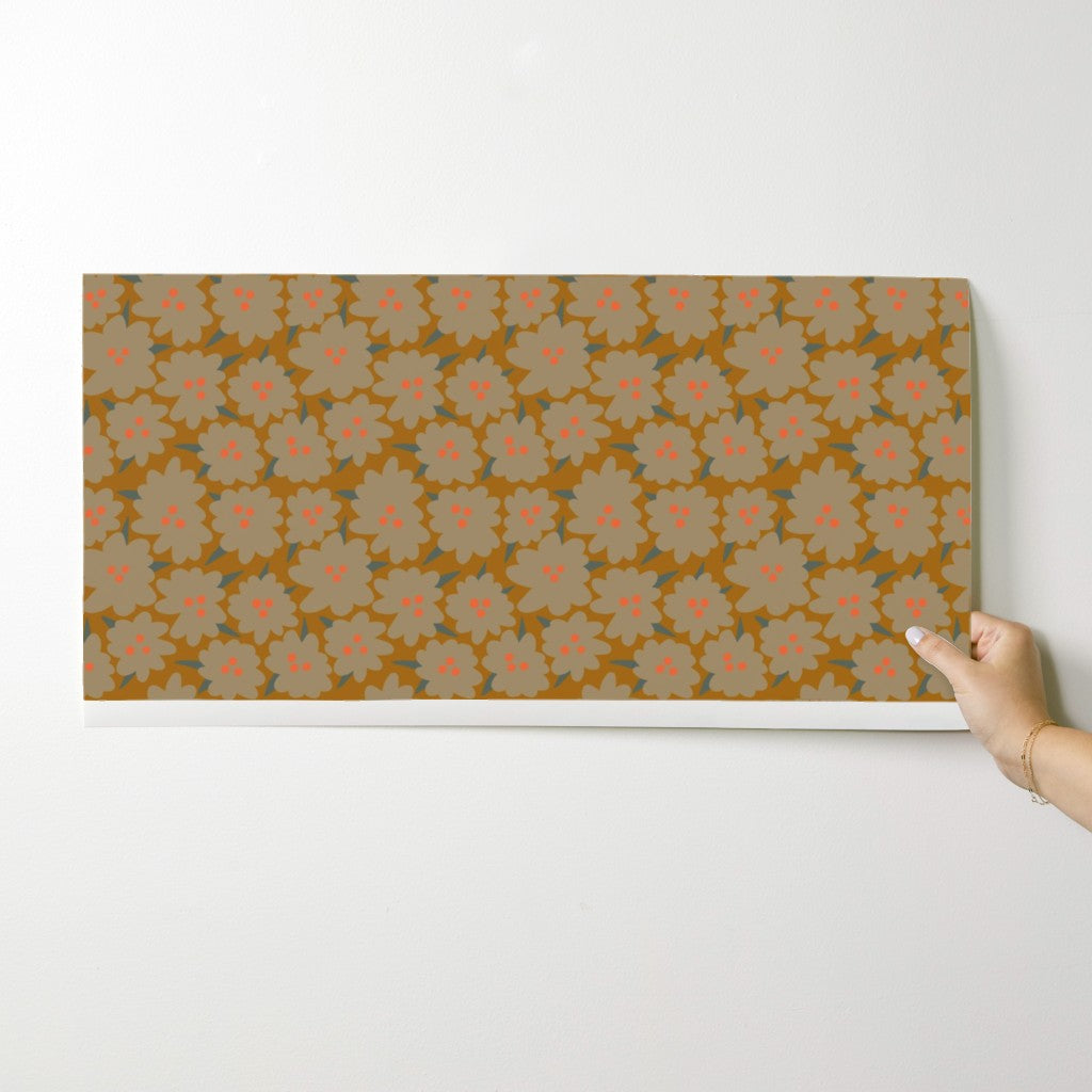 Floral patterned wallpaper swatch being held against a white wall. Designed by artist Leila Simon Hayes.
