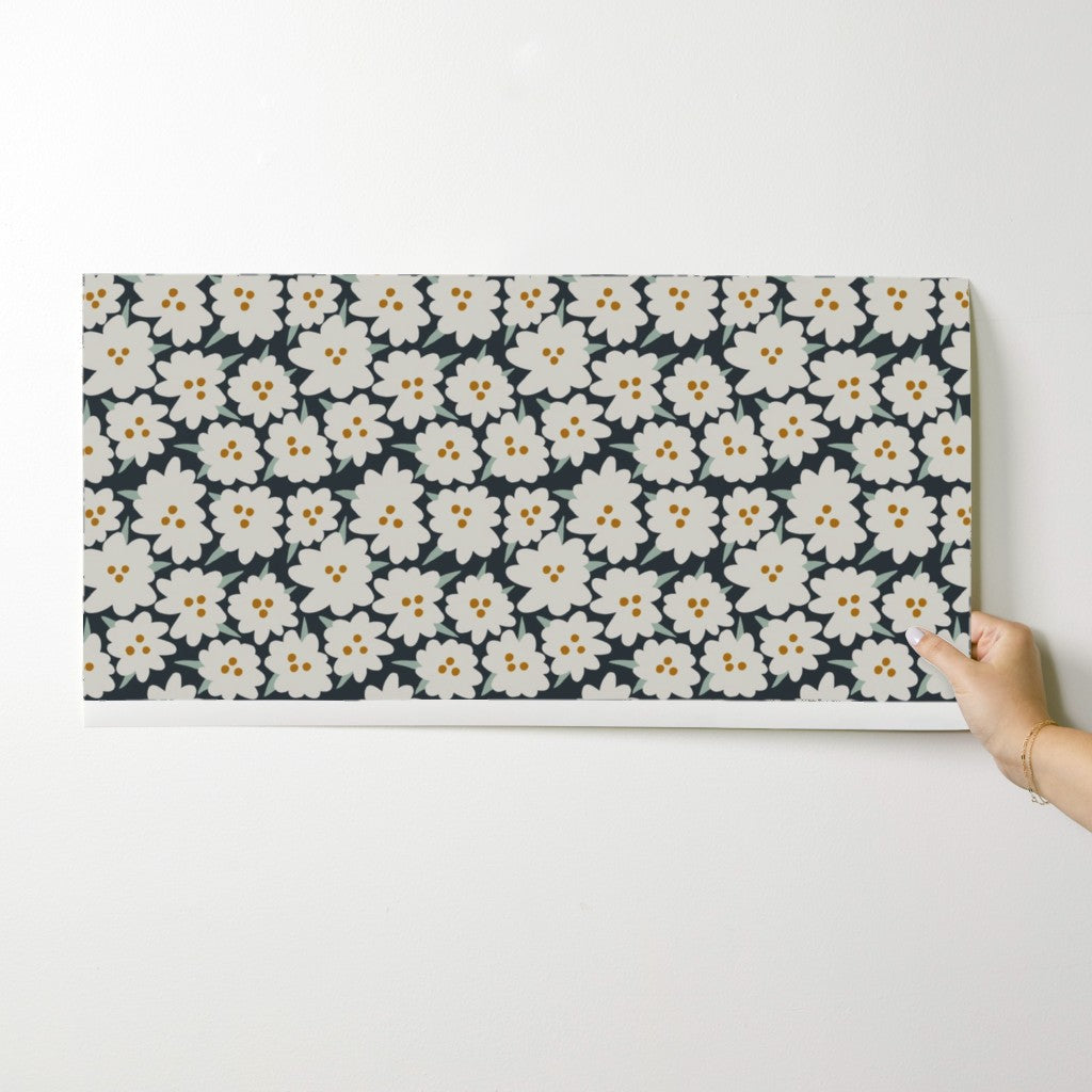 Floral patterned wallpaper swatch being held against a white wall. Designed by artist Leila Simon Hayes.