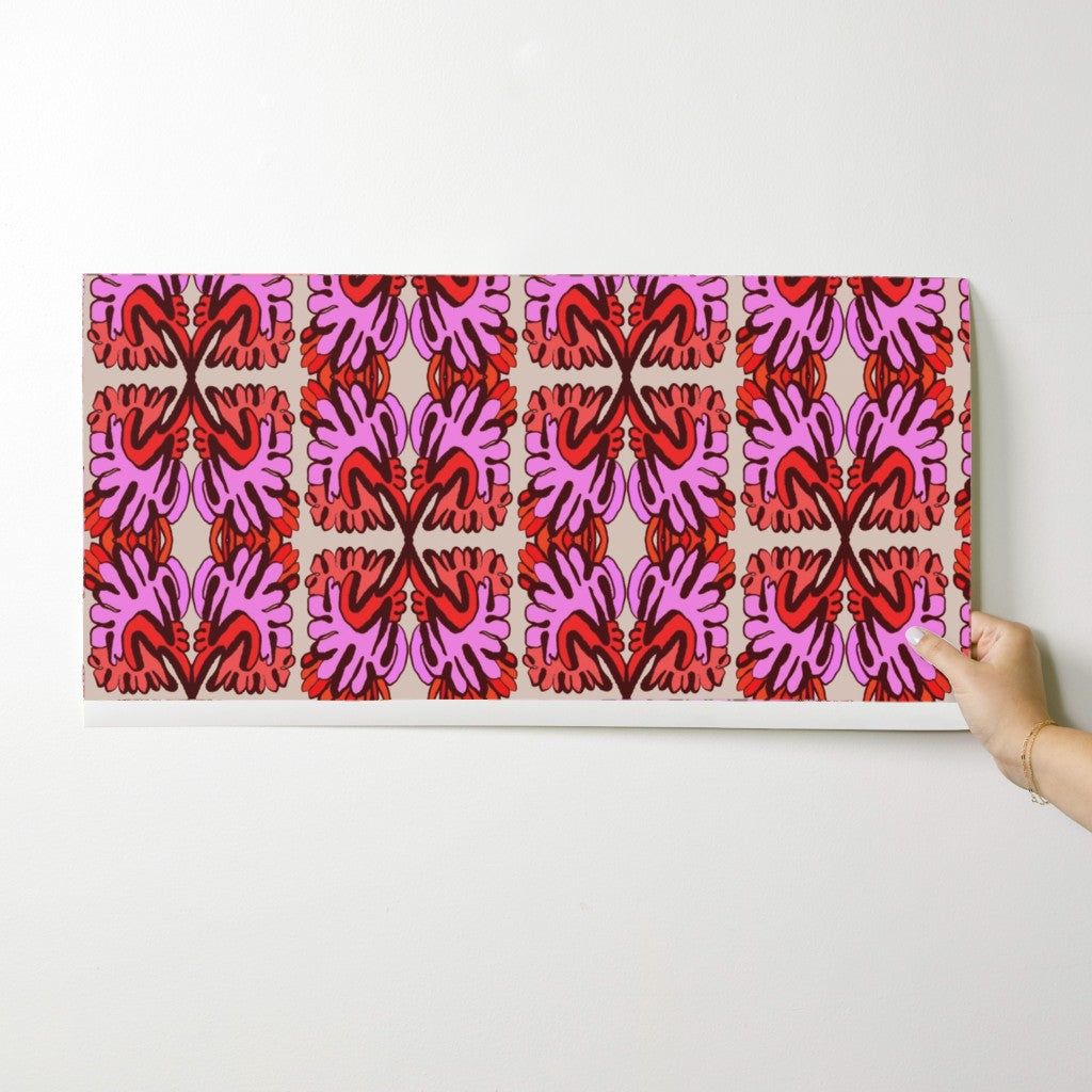 Hand holding a wallpaper swatch with a red and pink geometric pattern on a white background. Designed by artist Leila Simon Hayes.