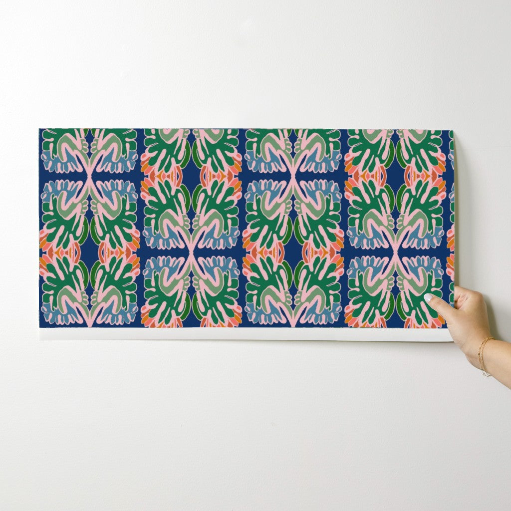 Hand holding a wallpaper swatch with a colorful pattern against a white background. Designed by artist Leila Simon Hayes. 