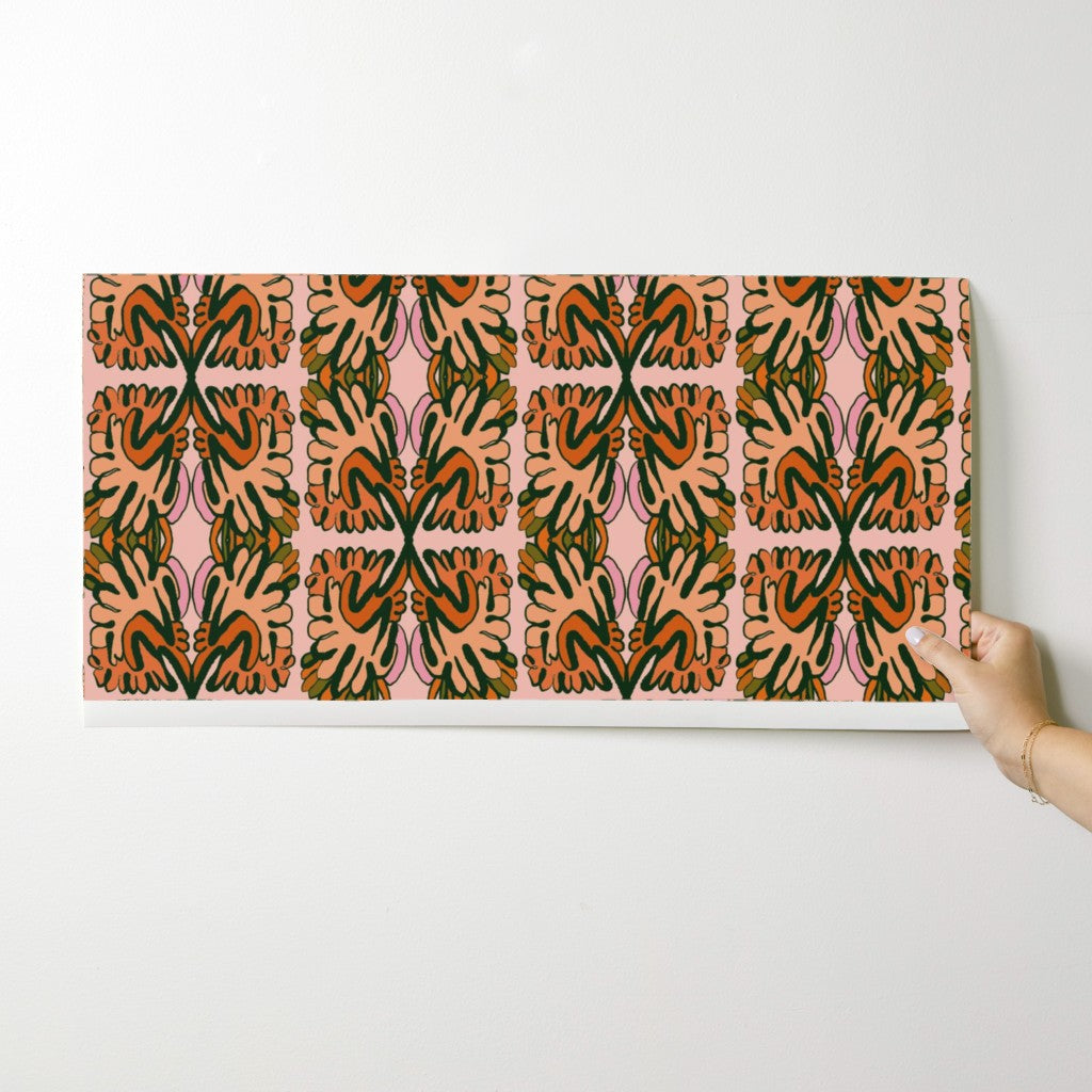 Hand holding a wallpaper swatch with a colorful geometric pattern on a white background. Designed by artist Leila Simon Hayes. 