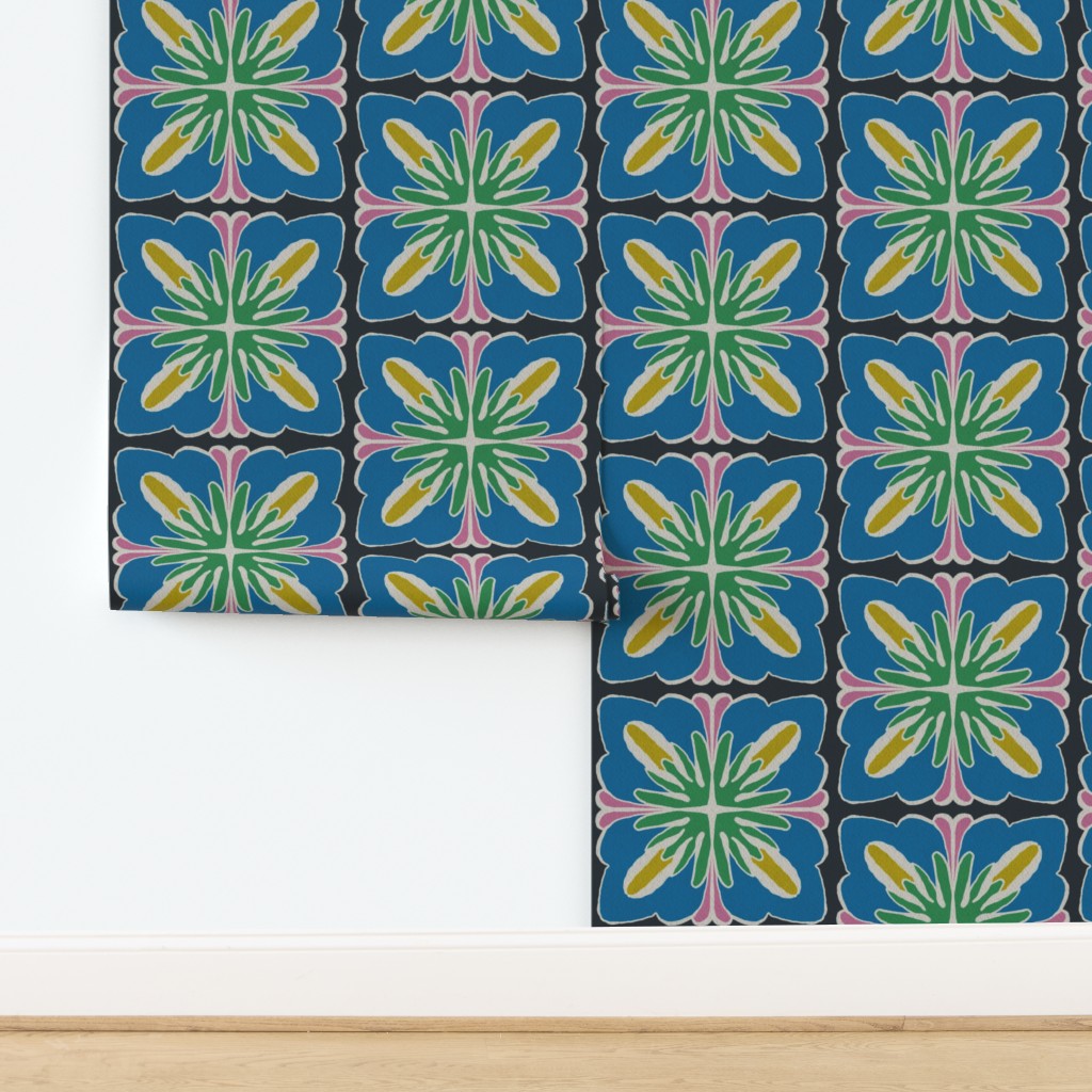 A close-up of patterned wallpaper or fabric with a repeating geometric floral tile design in blue, green, yellow, pink, and black, shown against a white wall and light wood floor. Designed by artist Leila Simon Hayes.