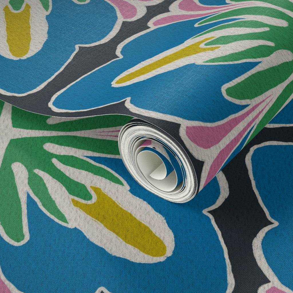 A close-up of a rolled sheet of wallpaper featuring a bold, retro-style floral pattern in bright blue, green, yellow, pink, and dark gray with white outlines. Designed by artist Leila Simon Hayes.