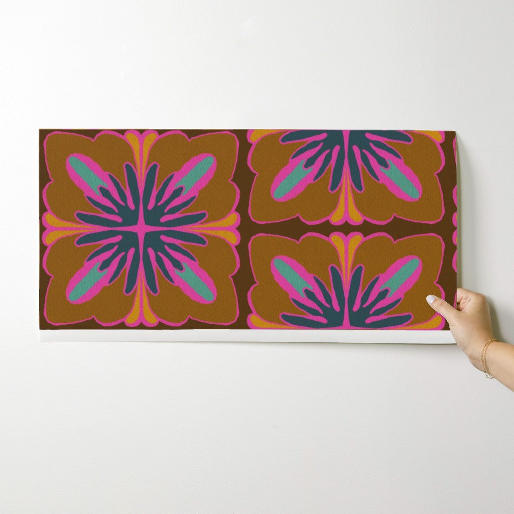 A rectangular wall art print with a retro floral pattern in brown, orange, pink, teal, and purple, shown hanging on a white wall with a hand holding the right edge. Designed by artist Leila Simon Hayes.
