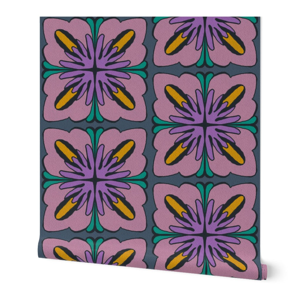 A roll of wallpaper featuring a retro 1970s-style floral pattern with pink petals, purple centers, yellow accents, and teal details on a dark slate blue background. Designed by artist Leila Simon Hayes.