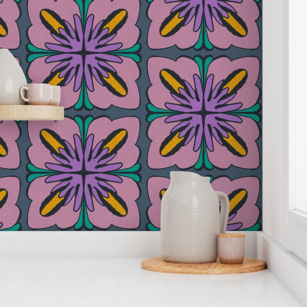 A styled interior scene showing a wall covered in a bold retro floral tile pattern in pink, purple, teal, yellow, and dark gray. A white shelf and countertop with ceramic pitchers, cups, and a wooden tray are placed in front of the wall. Designed by artist Leila Simon Hayes.