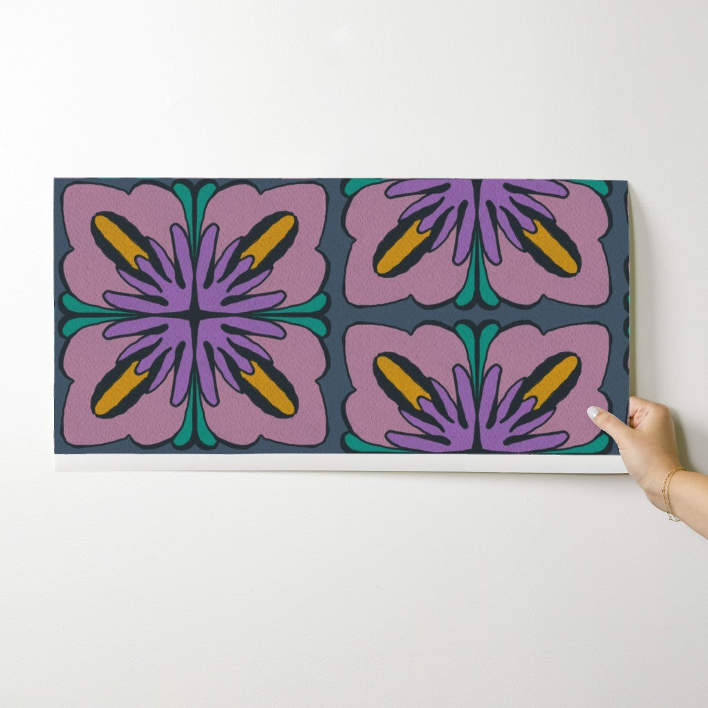 A rectangular wall art print or canvas with a retro floral pattern in purple, pink, yellow, and teal on a dark background, shown hanging against a white wall with a hand holding the right edge. Designed by artist Leila Simon Hayes.