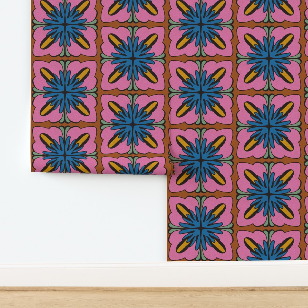 A folded piece of wallpaper or fabric with a retro 1970s floral pattern, displayed against a white wall and light wood floor. The pattern features blue and yellow starburst motifs on pink backgrounds with a brown grid. Designed by artist Leila Simon Hayes.