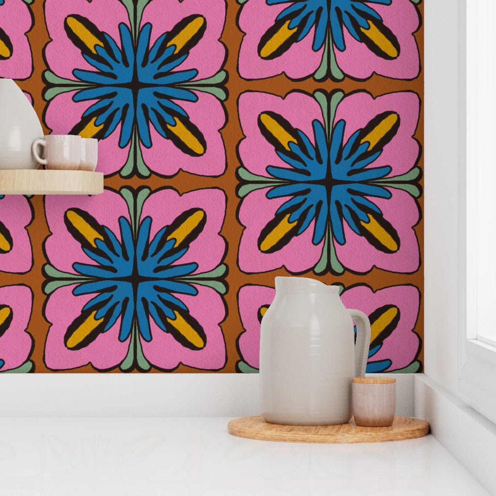 A retro-style floral wallpaper with a bold pink, blue, yellow, and brown pattern, shown on a kitchen backsplash behind a white ceramic pitcher and a small wooden tray. Designed by artist Leila Simon Hayes.