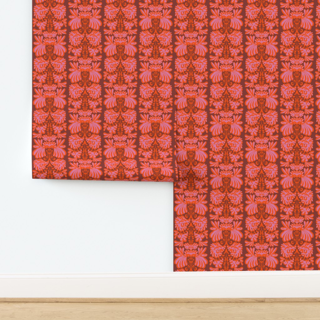 A roll of wallpaper with a repeating vertical damask-style pattern in pink, coral, and rust tones, shown partially unrolled on a white wall above a light wood floor. Designed by artist Leila Simon Hayes.
