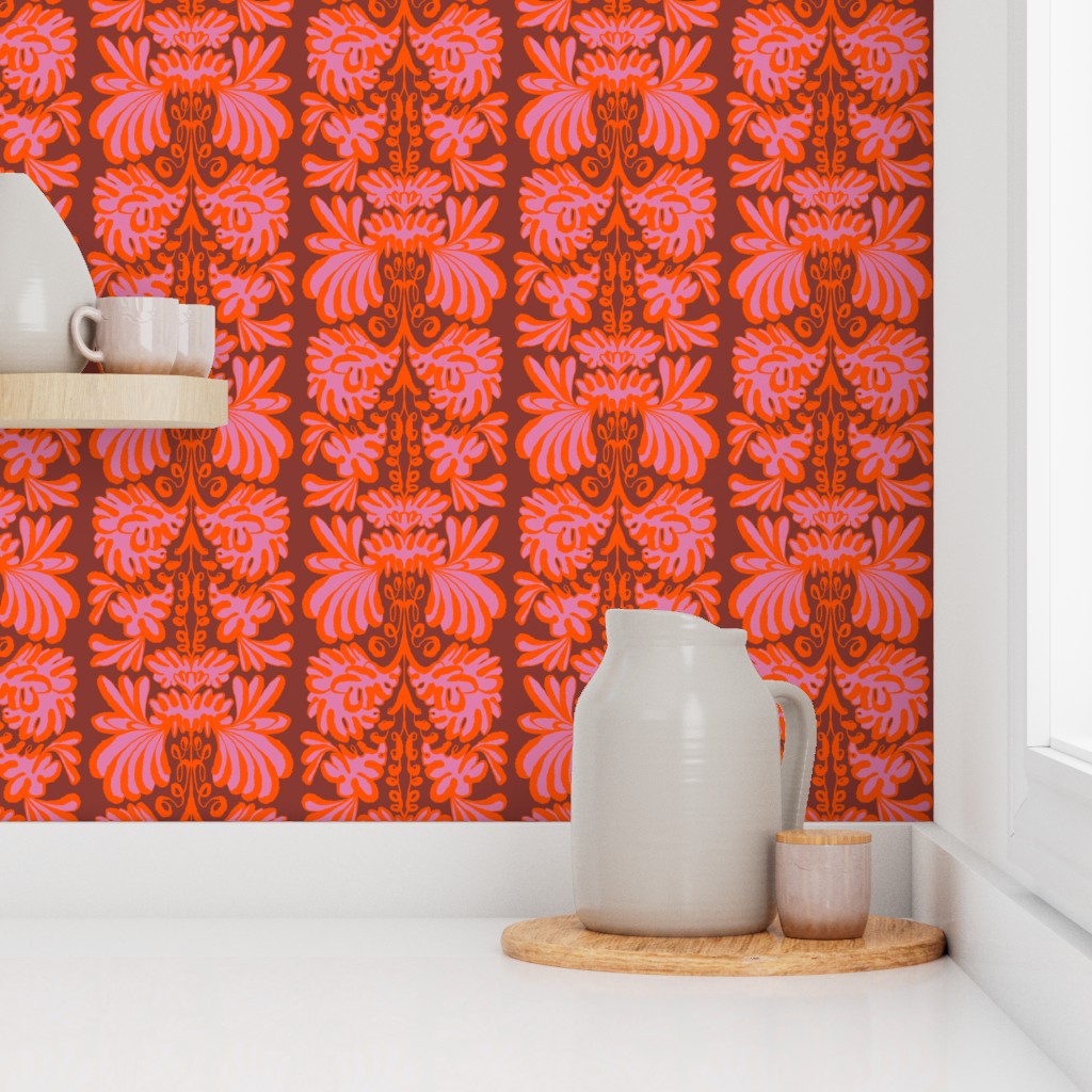 A kitchen countertop scene featuring a bold, repeating damask-style wallpaper in vibrant orange, red, and pink. On the white countertop, a light gray ceramic pitcher and a small cup sit on a round wooden coaster, with a matching shelf holding a white mug on the left. Designed by artist Leila Simon Hayes.