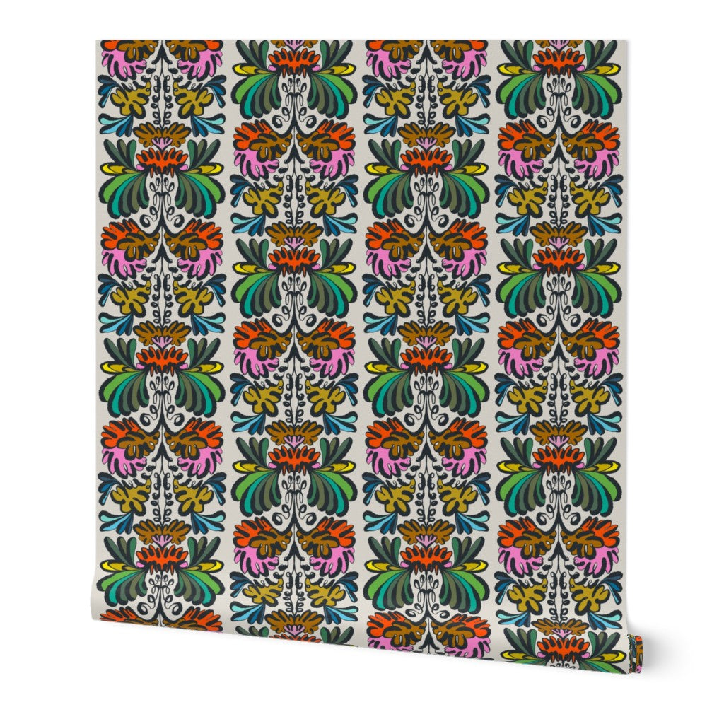 A roll of wallpaper with a vibrant, multicolored vertical damask pattern on a white background, shown slightly angled to reveal the roll's depth and a small yellow brand tag on the bottom right. Designed by artist Leila Simon Hayes.