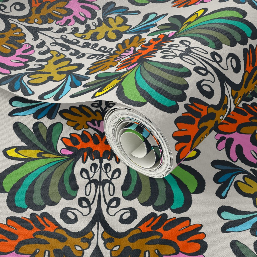 A roll of patterned wallpaper shown close up, featuring a retro 1970s floral design with bold orange, green, pink, blue, yellow, and black motifs on a white background. Designed by artist Leila Simon Hayes.