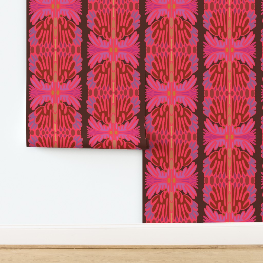 A folded piece of wallpaper with a bold vertical pattern of pink, red, and orange floral motifs on a dark brown background, displayed against a white wall and light wood floor. Designed by artist Leila Simon Hayes.