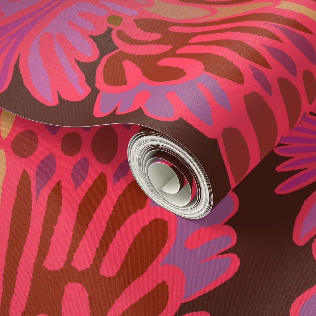 A close-up of a rolled sheet of patterned wallpaper or fabric with a bold retro floral design in pink, purple, brown, and rust tones on a white backing. Designed by artist Leila Simon Hayes.