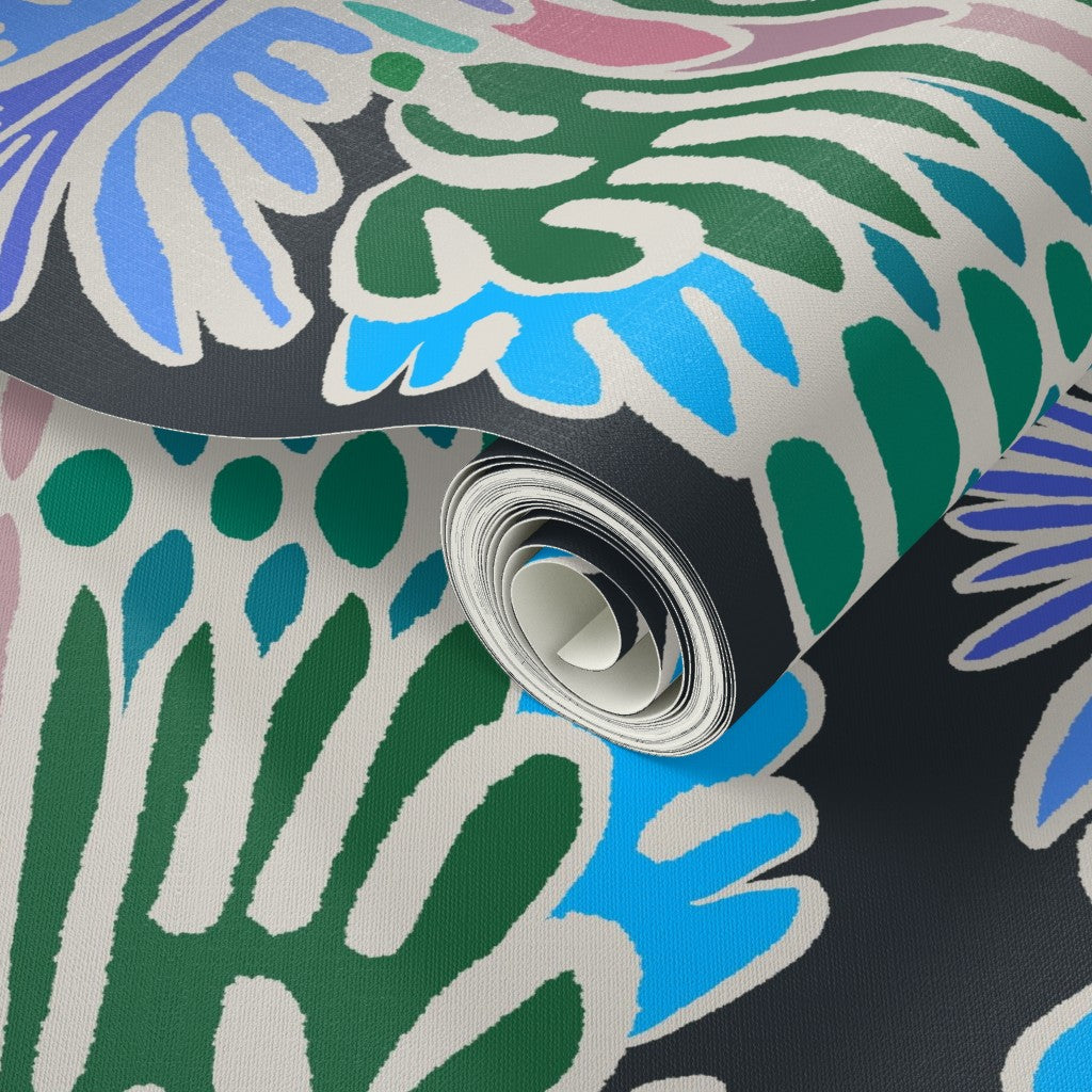 A close-up of a rolled sheet of patterned wallpaper or fabric with an abstract botanical design in green, blue, pink, and white over a dark charcoal background. Designed by artist Leila Simon Hayes.