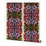 A roll of wallpaper featuring a bold, symmetrical mid-century modern pattern with pink, orange, teal, and olive green abstract leaf-like motifs on a cream background. Designed by artist Leila Simon Hayes.