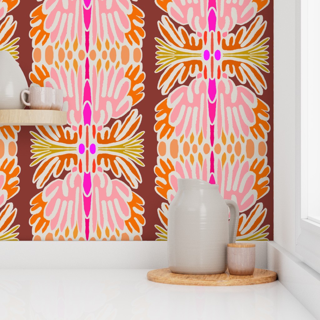 A styled interior scene showing a wall covered in bold retro floral wallpaper with pink, orange, yellow, and white motifs on a brown background. A white ceramic pitcher and small cup sit on a round wooden tray on a white countertop, with a shelf and white wall visible. Designed by artist Leila Simon Hayes.