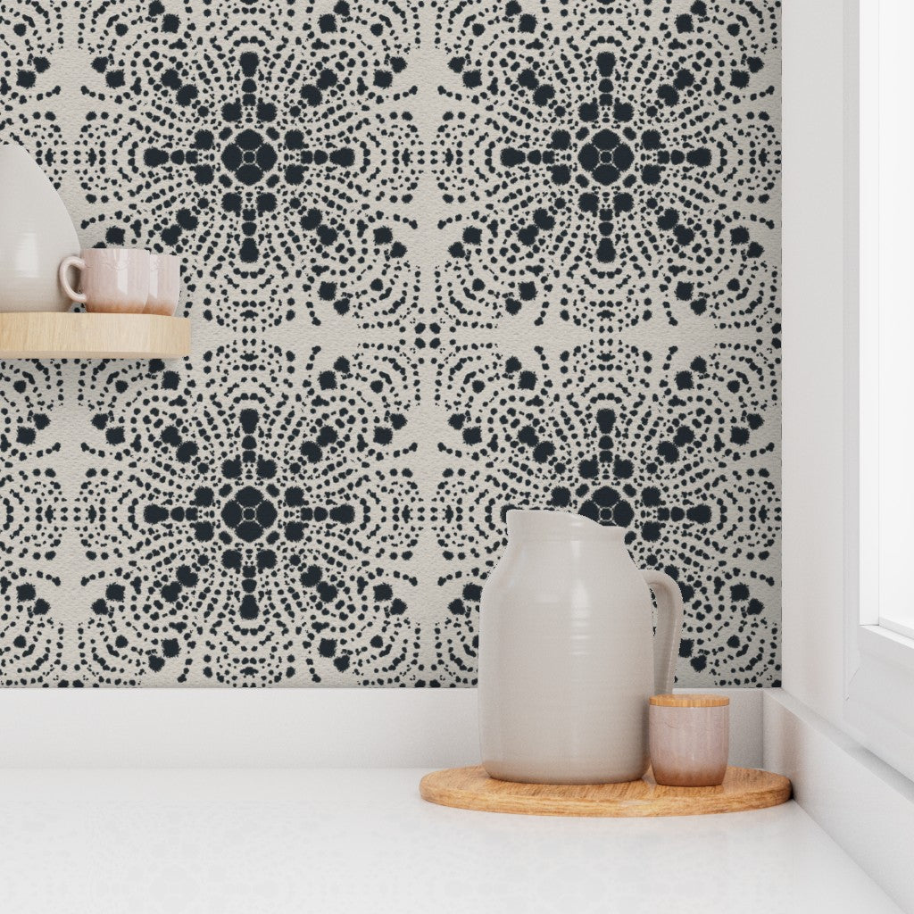 Black and white patterned wallpaper with a repeating medallion design, shown on a kitchen backsplash behind a white countertop with a ceramic pitcher and small cup on a wooden tray. Designed by artist Leila Simon Hayes.