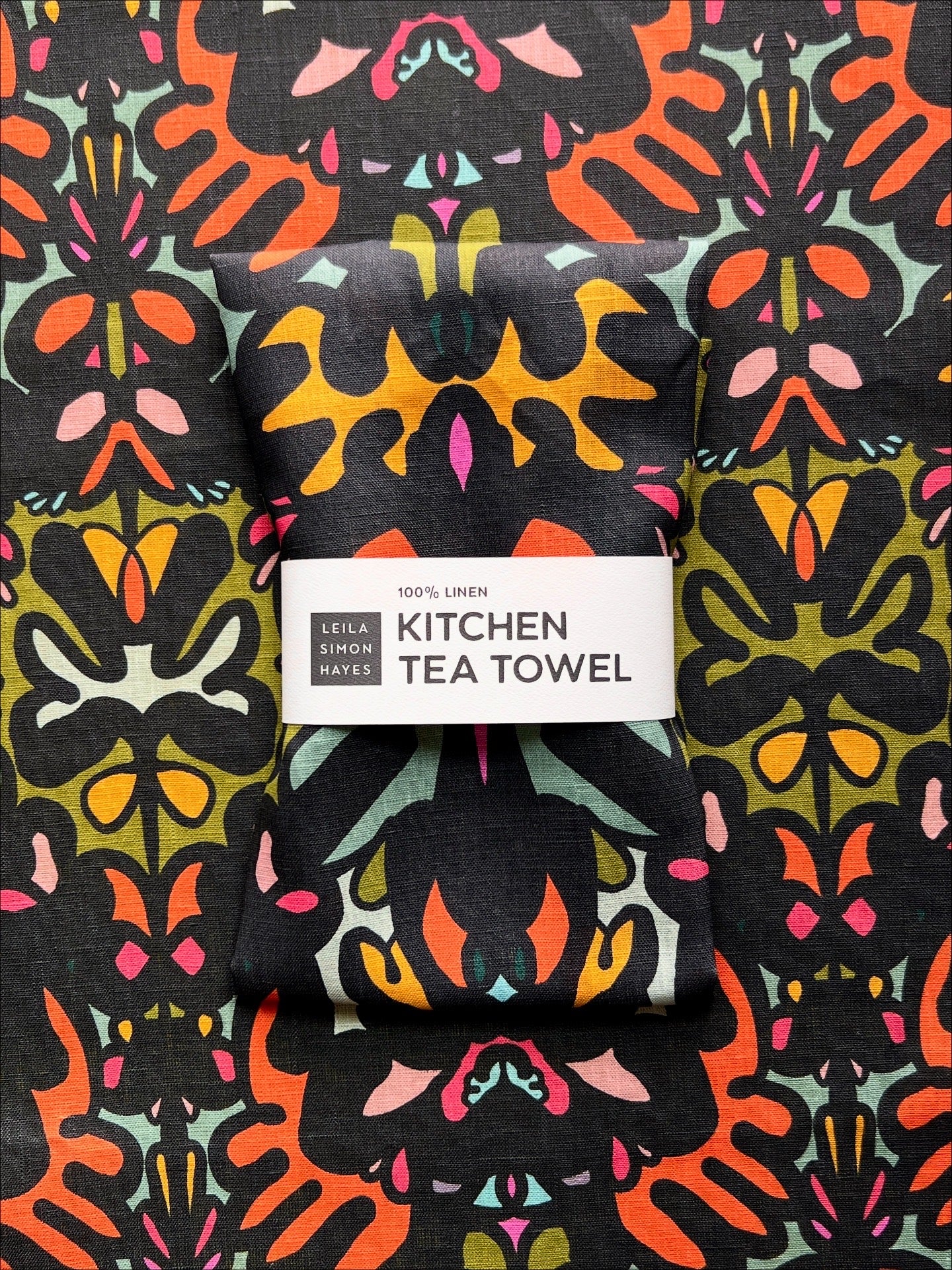 Colorful kitchen tea towel with a pattern and '100% Linen' label on a matching background. Designed by artist Leila Simon Hayes.