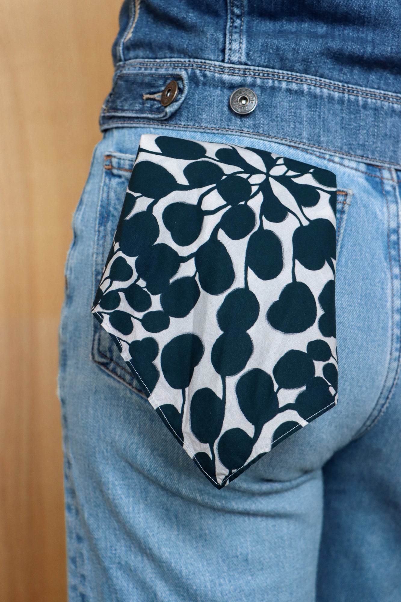 Blue jeans with a floral patterned pocket on a wooden surface. Designed by artist Leila Simon Hayes.