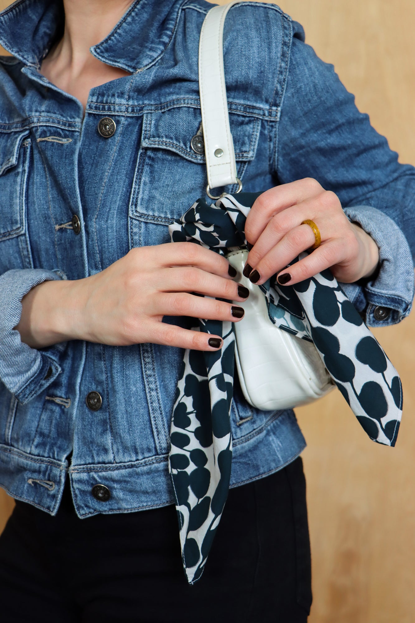 Person holding a white handbag with a black and white patterned strap against a beige background. Designed by artist Leila Simon Hayes.