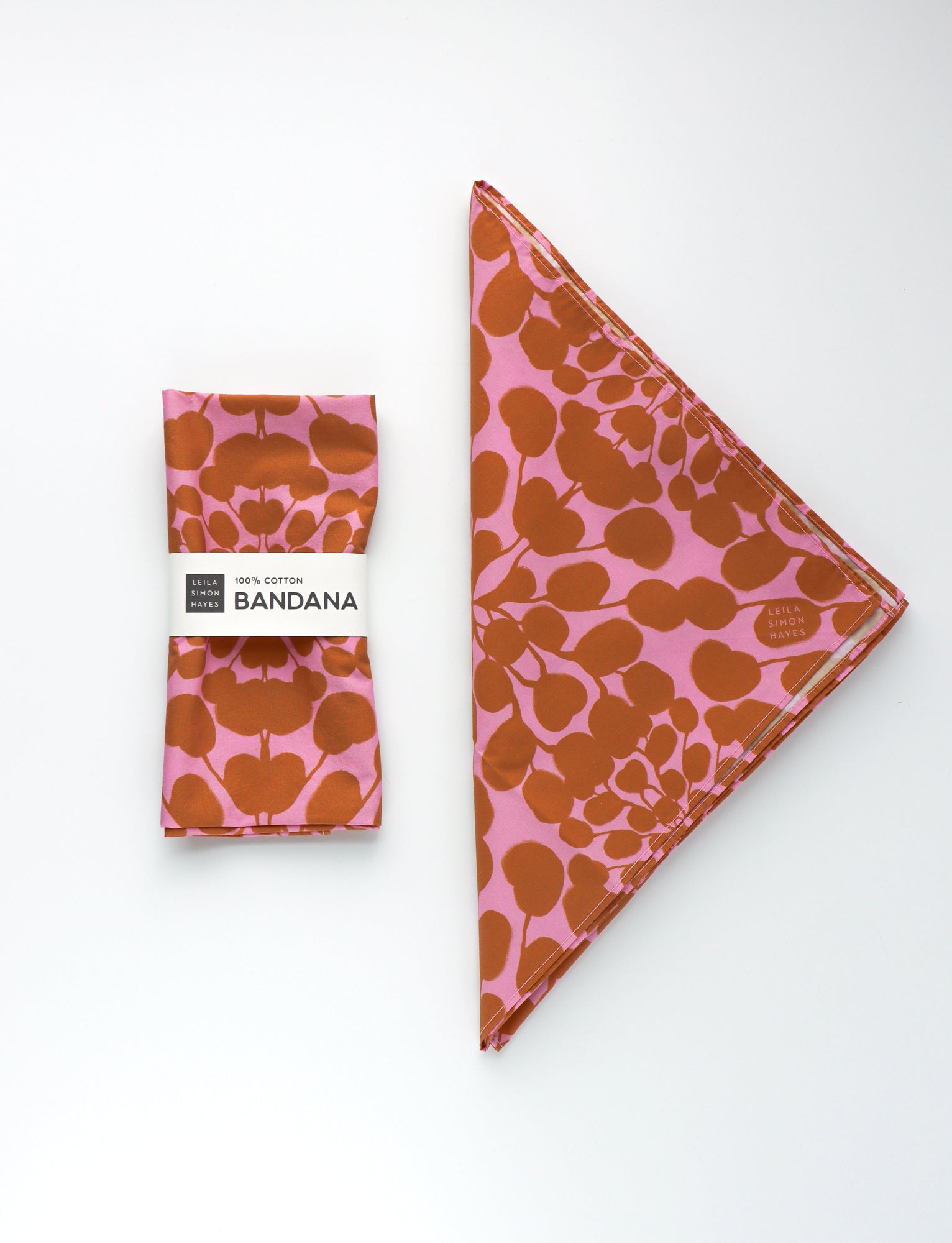 Pink bandana with brown floral pattern and packaging on a white background. Designed by artist Leila Simon Hayes.