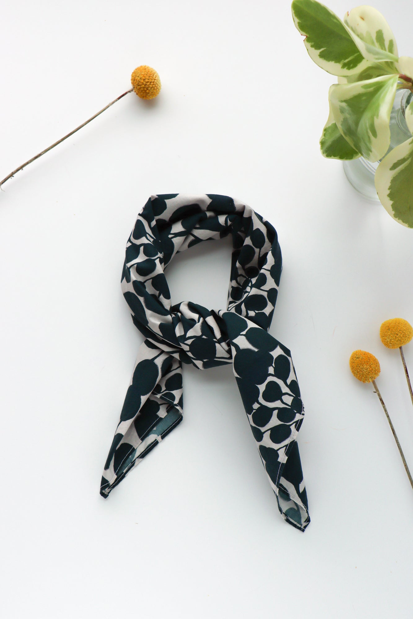 Black and white floral patterned bandana tied into a scarf on a white surface with decorative elements.Designed by artist Leila Simon Hayes.
