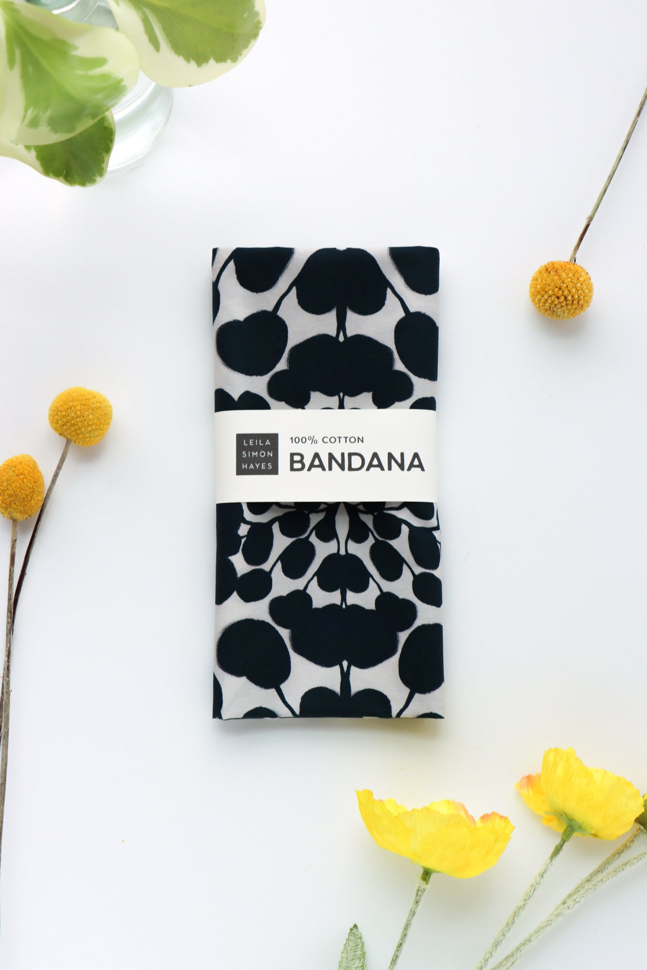 Black and white bandana with floral pattern on a white background with yellow flowers. Designed by artist Leila Simon Hayes.