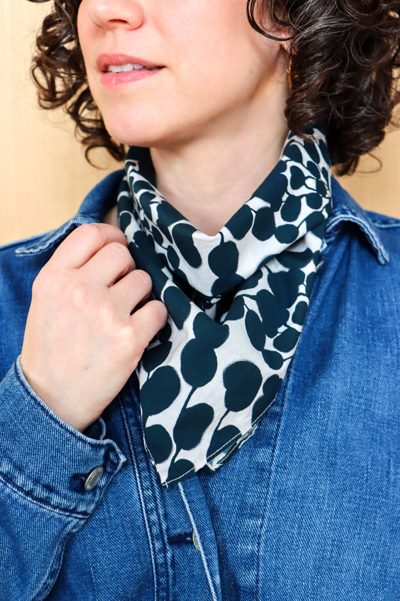 Person wearing a black and white patterned bandana tied into a scarf with a beige background. Designed by artist Leila Simon Hayes.