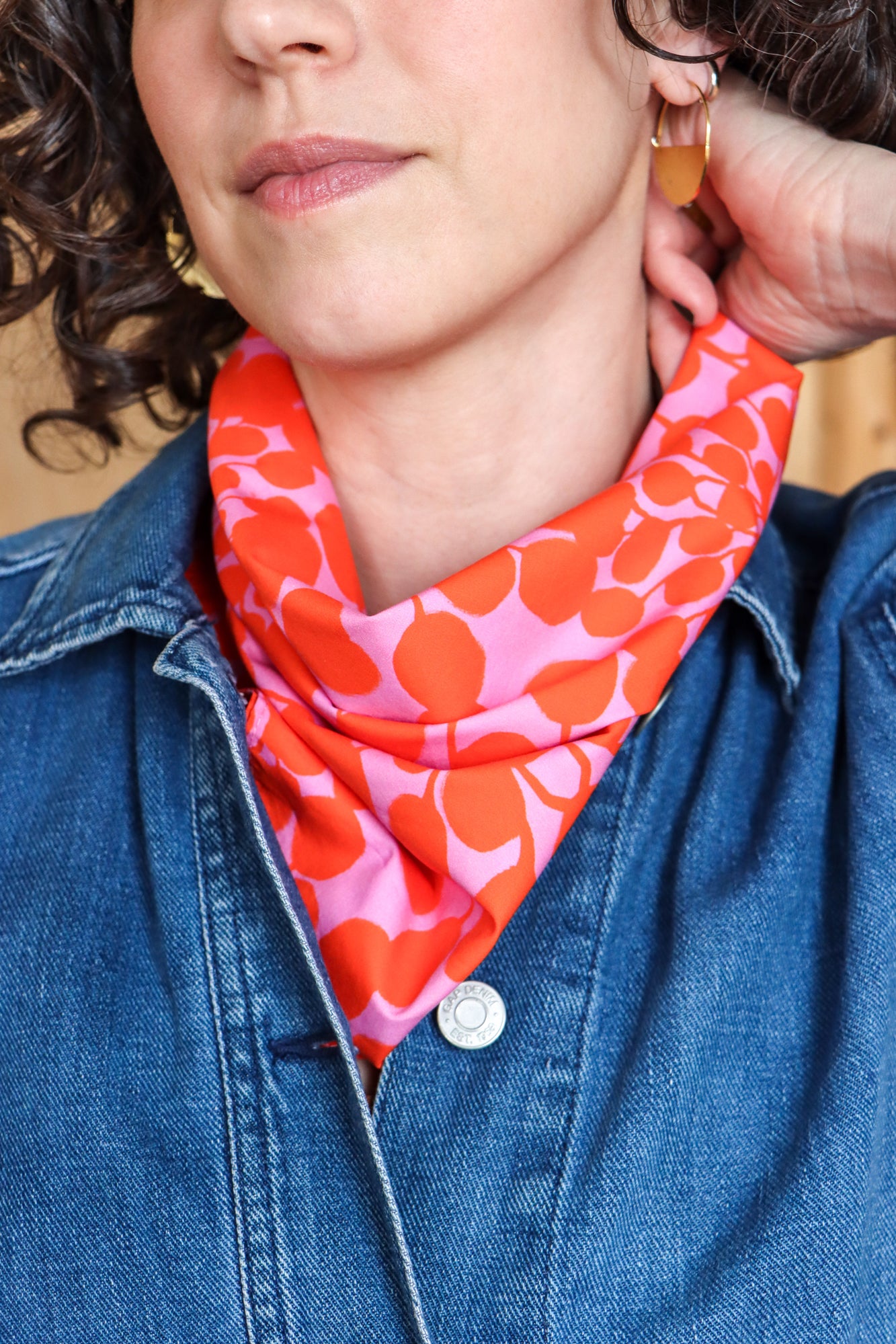Person wearing a colorful patterned bandana tied into a scarf and blue jacket. Designed by artist Leila Simon Hayes.